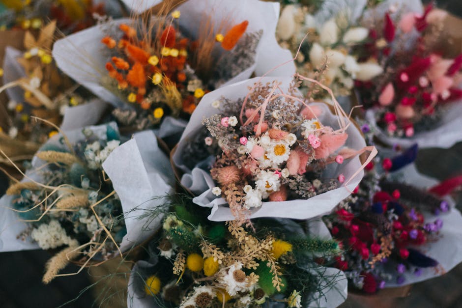 A collection of floral bouquets arranged with a variety of fresh flowers in vibrant colors, including pastel pinks, whites, soft yellows, with some dried and preserved elements, wrapped in white and t